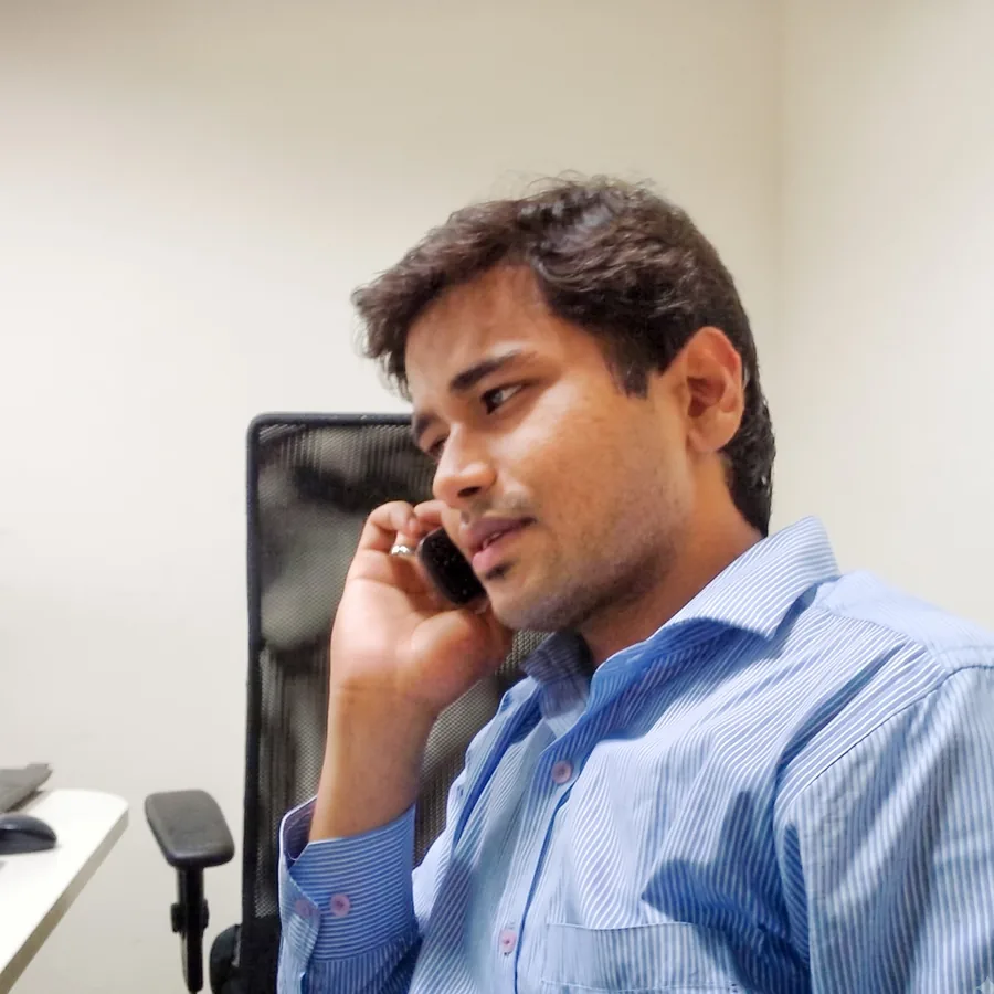 Lavi on a phone call at an office desk, in a blue striped shirt, with a laptop beside him.