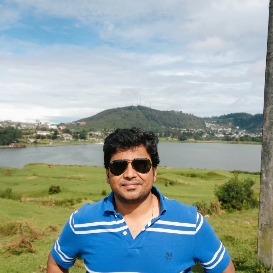 Lavi in sunglasses by a lake with green hills behind