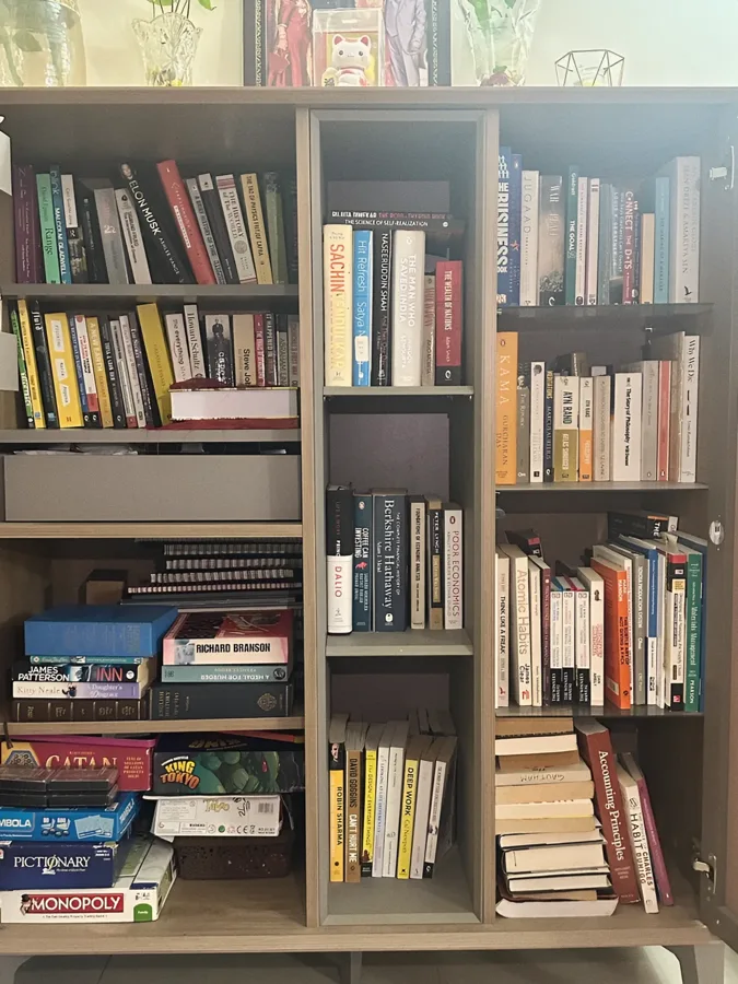 A bookshelf at home packed with books, with board game boxes stacked on the lower shelves