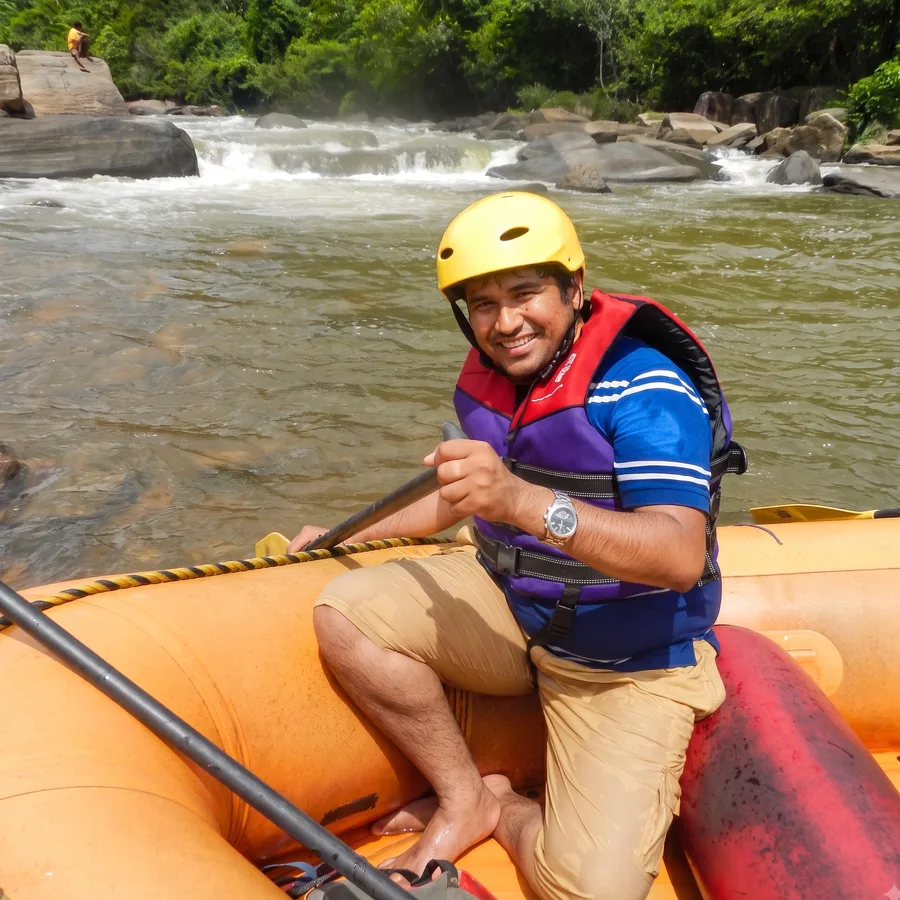 Lavi in a helmet and life jacket, paddling a raft through white water