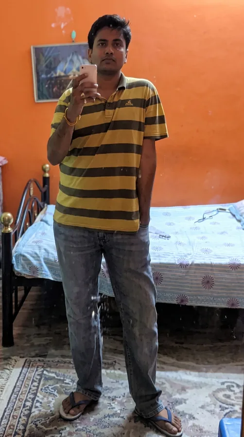 Lavi stands in a striped polo holding up a glass in a room with an orange wall.