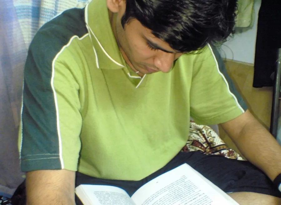 Lavi in a green polo reads an open book on his bed.