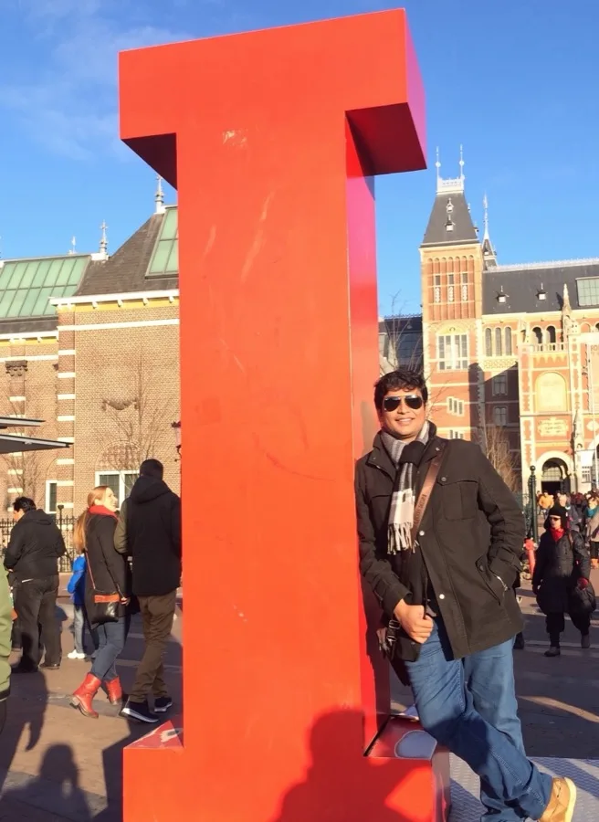 Lavi stands beside the giant red I letter with Amsterdam buildings behind.