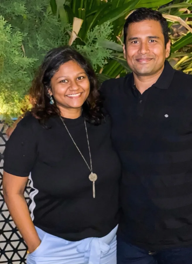 Lavi and a woman pose together in front of green leaves.