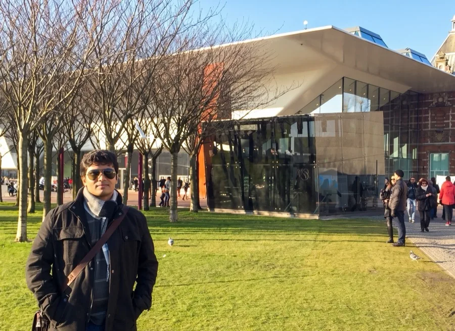 Lavi stands on a lawn in front of a modern museum building.