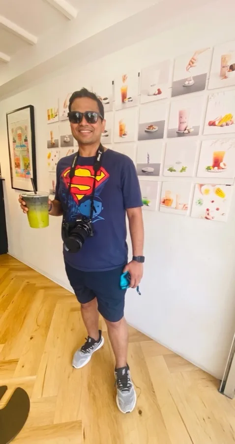 Lavi in a Superman tee stands in a bright hall with prints on the wall.