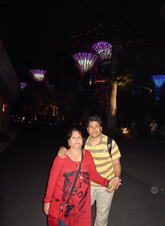 Lavi and a woman pose at night with glowing garden structures behind.