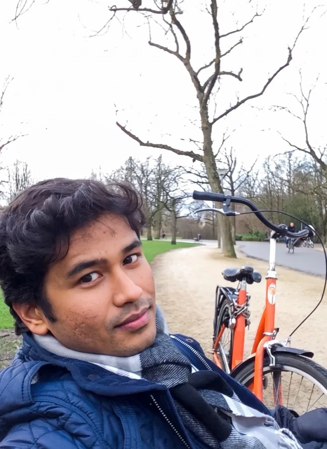 Lavi takes a selfie beside a bicycle on a path under bare trees.