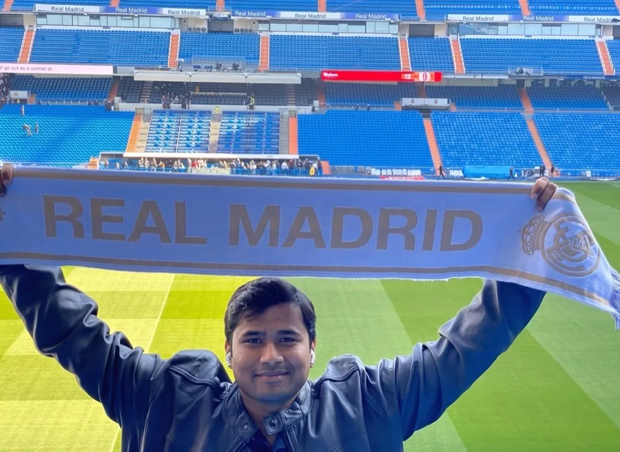 Lavi holds up a Real Madrid scarf in the stands of a football stadium.