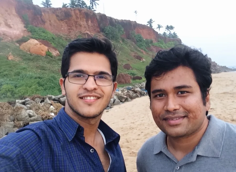 Lavi takes a selfie with a friend on a beach below red cliffs.