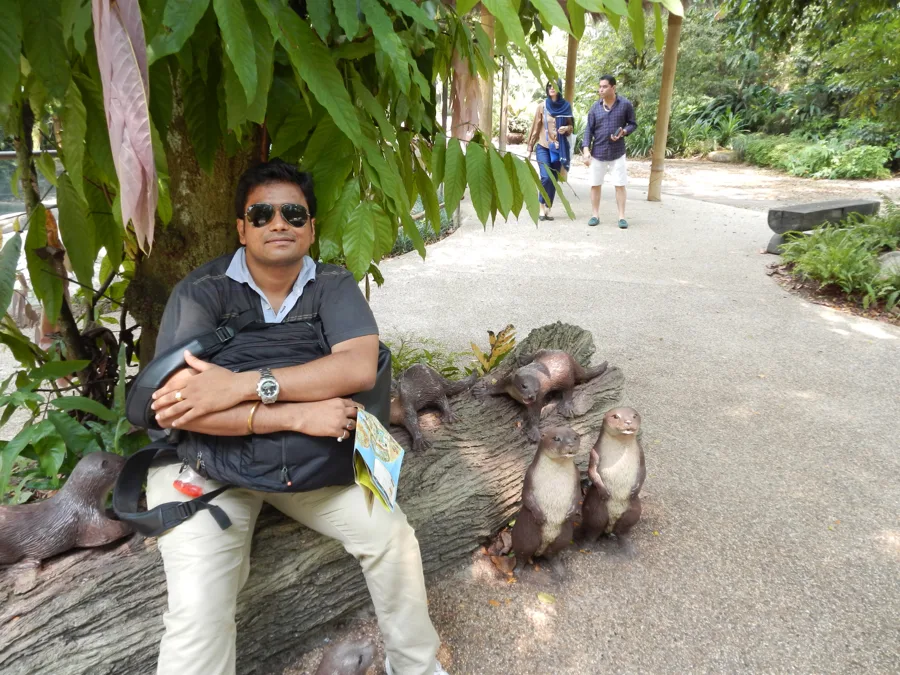 Lavi in sunglasses sits on a log with arms folded in a leafy garden path.